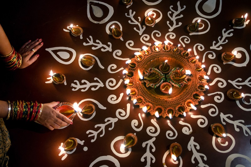 Woman arranging oil lamps on rangoli during Diwali