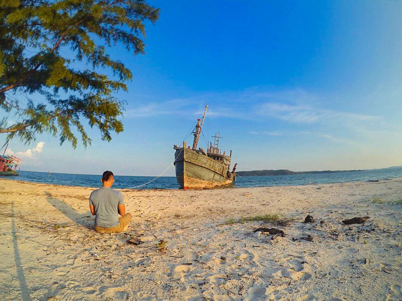 man sitting by shipwreck at pulau tunjuk